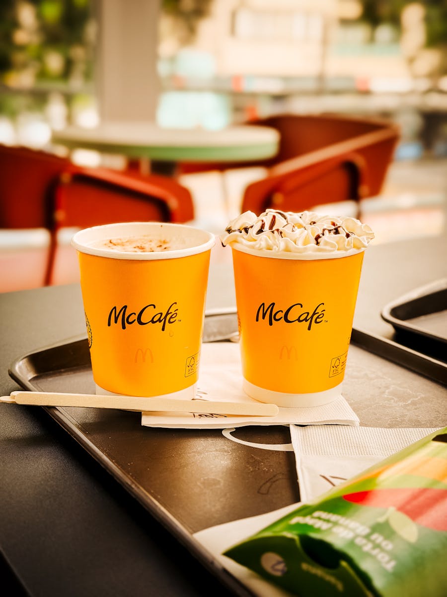 Two McCafé cups with whipped cream and napkins on a tray, highlighting dessert beverages in a São Paulo café.