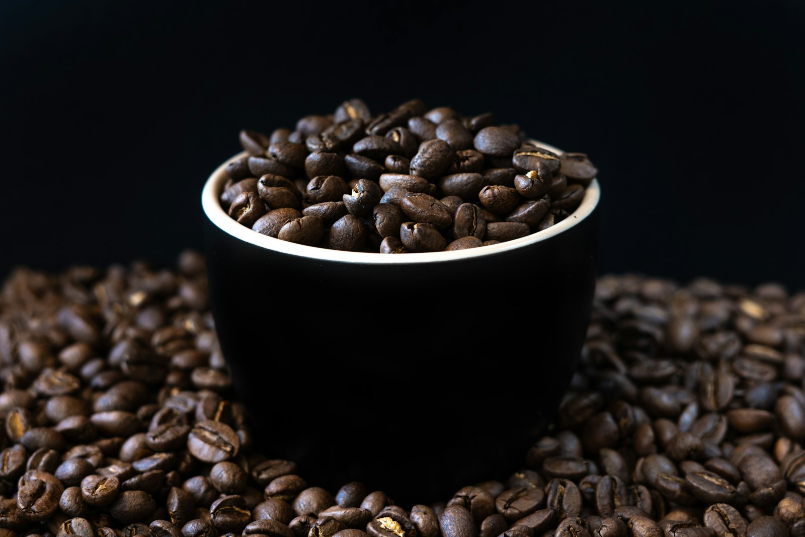 a black cup filled with coffee beans on top of a pile of coffee beans